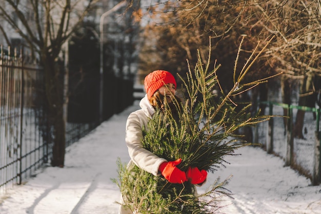 Een mooi meisje met een rode hoed draagt een kerstboom Minimaal mode feestelijk kerst- en nieuwjaarsconcept