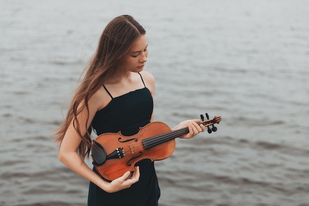 Een mooi meisje met een viool staat tegen de achtergrond van water. Aziatische uitstraling. muzikaal begrip. Hoge kwaliteit foto