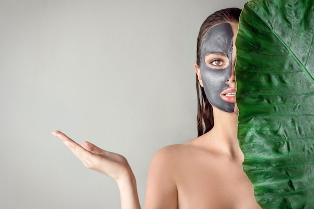 Een mooi meisje met een vochtinbrengend masker van klei en een groen blad vast te houden. spa.