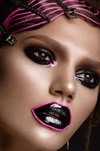 Een mooi meisje met een zwarte creatieve make-up en een roze draad op haar lippen Beauty face