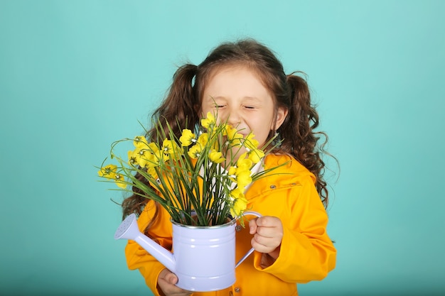 een mooi meisje met krullend haar in een geel jasje houdt een gieter met bloemen vast