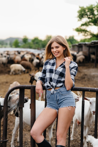 Een mooi meisje poseert op een boerderij met geiten en andere dieren. Landbouw, veeteelt.