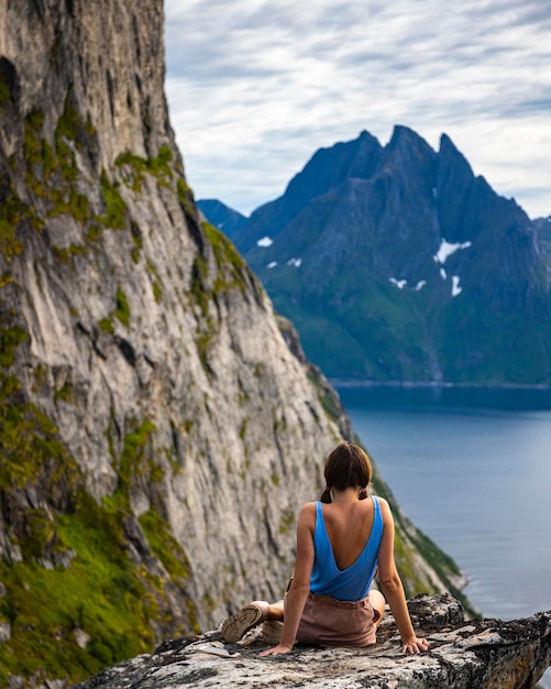 een mooi meisje zit op de rotsen en geniet van het uitzicht op de beroemde segla-berg in noorwegen, senja