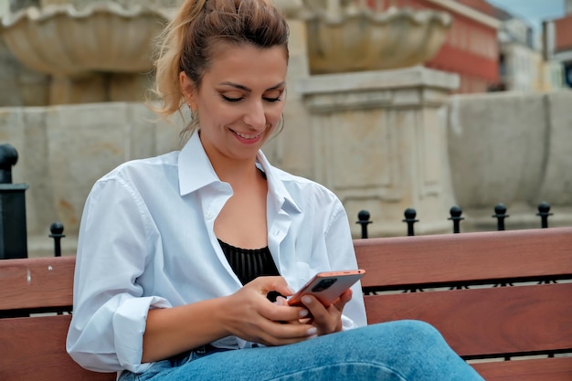 Een mooi meisje zit op een bankje en houdt een telefoon in haar handen het meisje bestelt eten via de telefoon het meisje praat aan de telefoon lachend blij verrast