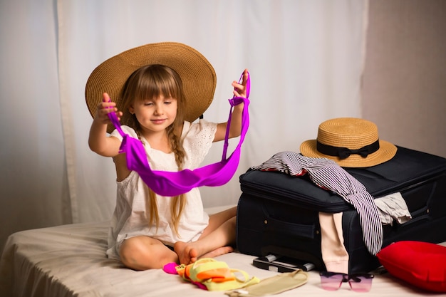 Een mooi meisje zit op het bed en bereidt bagage voor op een reis kleren aanbrengend een koffer dromen van een vakantie