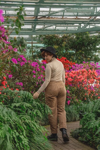 Een mooi plus size meisje in een hoed glimlacht tussen de groene planten van de kas