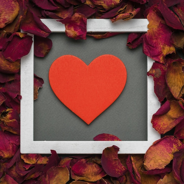 Een mooi rood hart in een wit frame met rozenblaadjes op een grijze achtergrond. Het concept van een romantische relatie. Plat leggen.