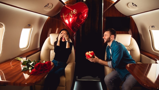 Een mooi stel viert Sint-Valentijnsdag in een privéjet. Een man geeft een cadeau in een rode doos aan zijn vriendin