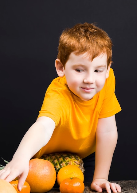 Een mooie aangename roodharige jongen met citrusvruchten grapefruit waaruit sap of ander voedsel wordt bereid, de jongen is blij om te eten en te spelen met citrusvruchten op tafel, zure citrus