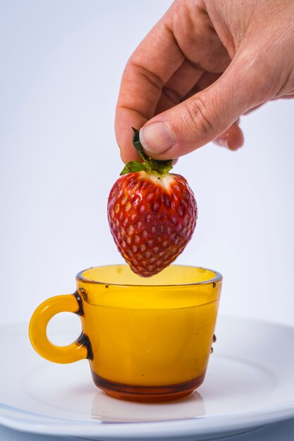 Een mooie aardbei die door een vrouwenhand in een kop van melk onderdompelt