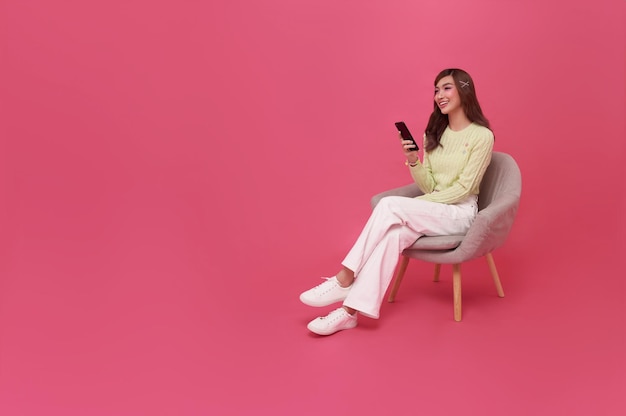 Een mooie Aziatische tienervrouw die een smartphone gebruikt en op een stoel zit.