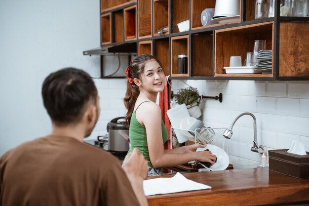 Foto een mooie aziatische vrouw die afwas terwijl ze met haar partner in de keuken praat.