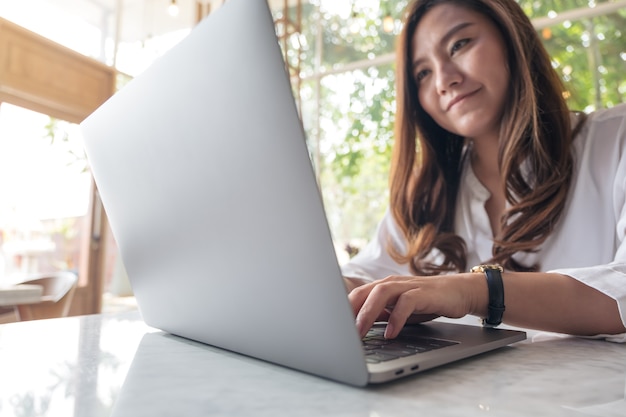 een mooie Aziatische vrouw die en op laptop in koffie gebruikt typt