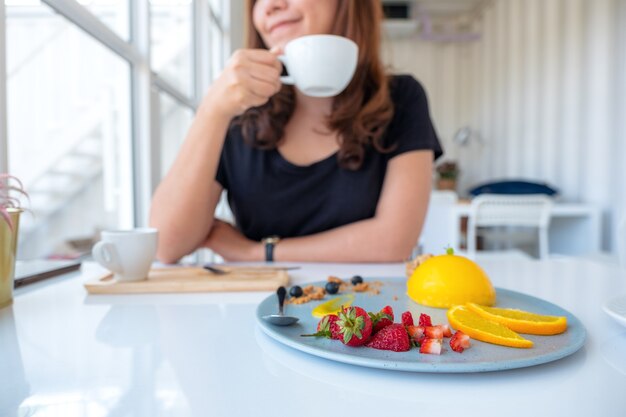 Een mooie aziatische vrouw die koffie drinkt en oranje cake met gemengd fruit eet in koffie