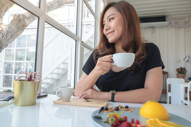 Een mooie Aziatische vrouw die koffie drinkt en oranje cake met gemengd fruit eet in koffie