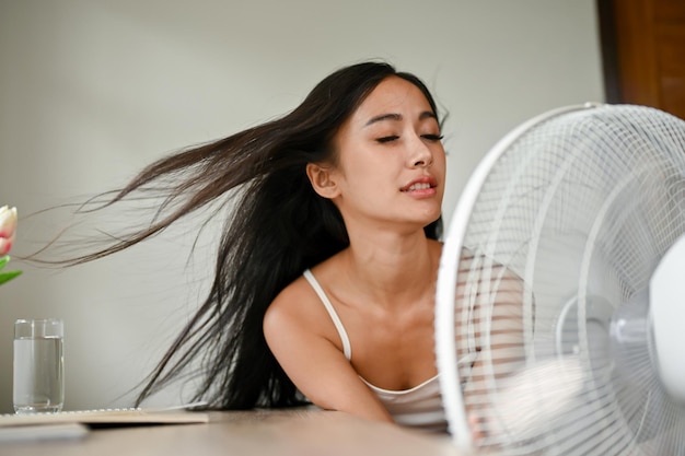 Foto een mooie aziatische vrouw die oververhit raakt, koelt zichzelf af met een elektrische ventilator