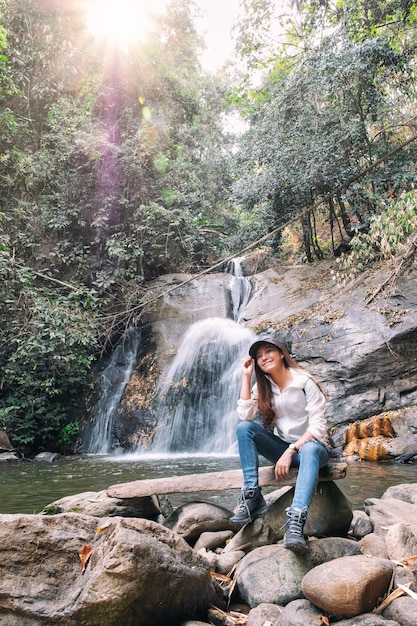 Een mooie Aziatische vrouw die voor een waterval in de jungle zit