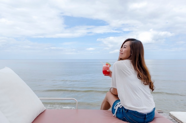 Een mooie Aziatische vrouw die watermeloensap drinkt terwijl ze aan zee zit