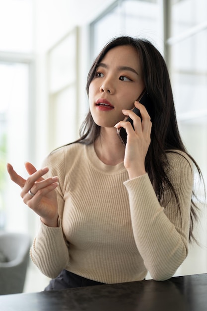 Een mooie Aziatische vrouw heeft een serieus telefoongesprek terwijl ze binnen aan een tafel zit.