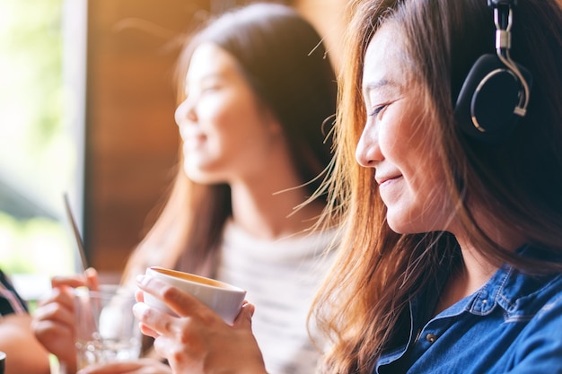 Een mooie Aziatische vrouw luistert graag naar muziek met een koptelefoon terwijl ze koffie drinkt met vrienden