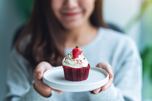 Een mooie Aziatische vrouw met een bord rode fluweel cupcake.