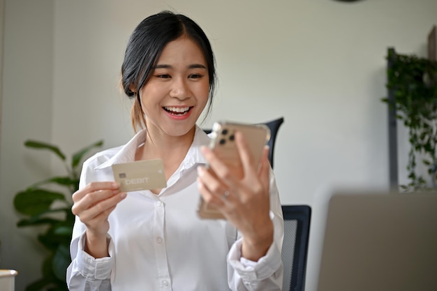 Een mooie Aziatische vrouw met een smartphone en een creditcard die online winkelt.