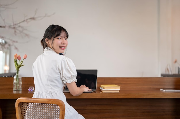 Een mooie Aziatische vrouw zit aan een tafel in een koffieshop met haar laptop op tafel en werkt op afstand