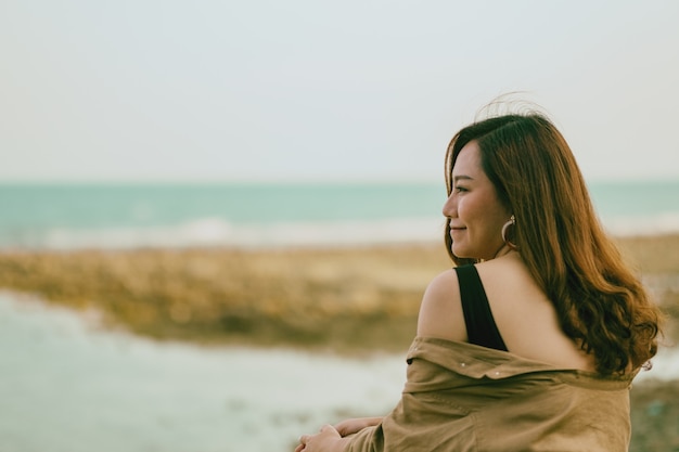 Een mooie Aziatische vrouw zit graag op de rots aan de kust