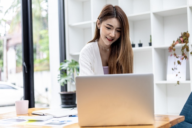 Een mooie Aziatische zakenvrouw die in een kamer staat, ze praat zaken met haar partner via een laptop-boodschapper, ze is een vrouwelijke directeur van een startend bedrijf. Concept van financieel beheer