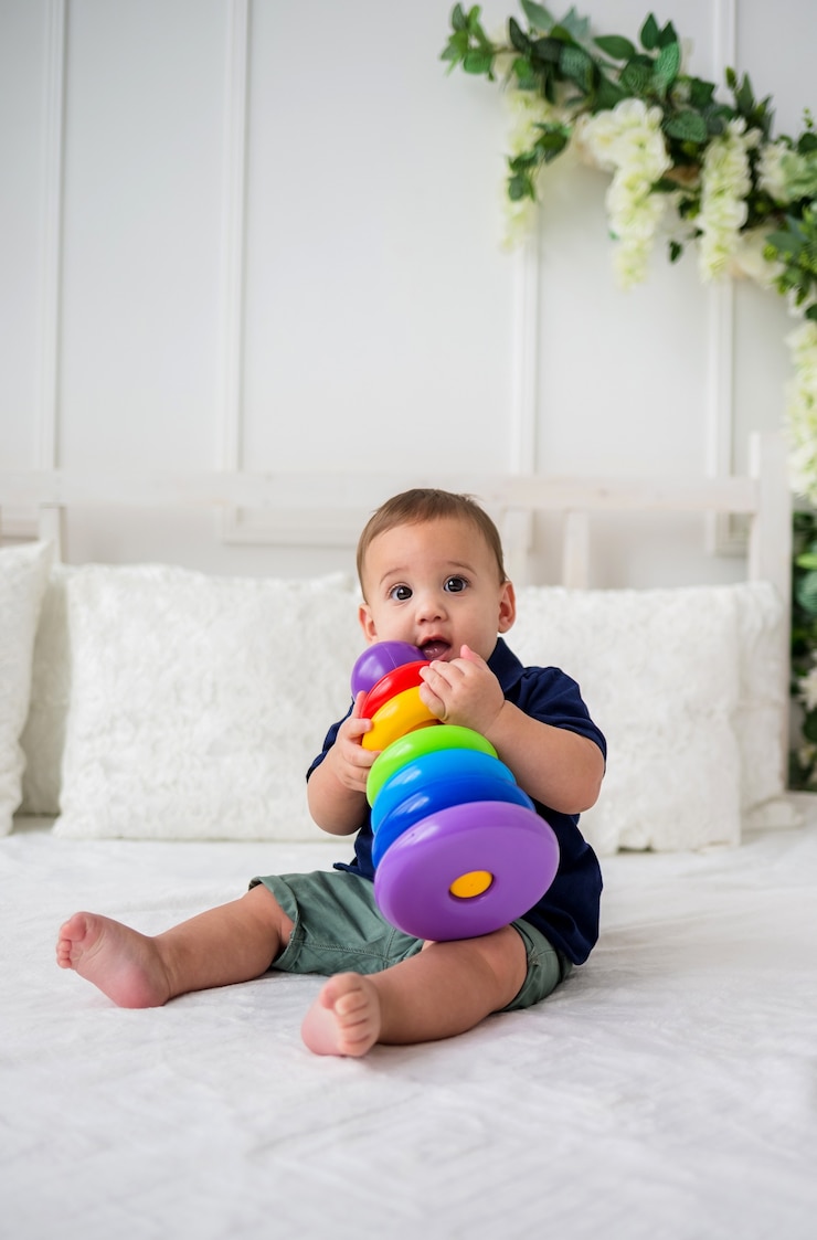 Foto een mooie babyjongen zit op een wit bed en speelt met een piramidespeelgoed