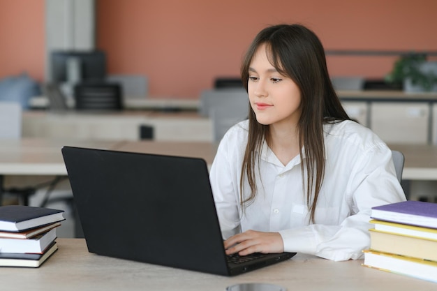 Een mooie blanke studente studeert op afstand op de universiteit Ze zit met een laptop en een notitieblok en kijkt geconcentreerd naar een videoconferentieles
