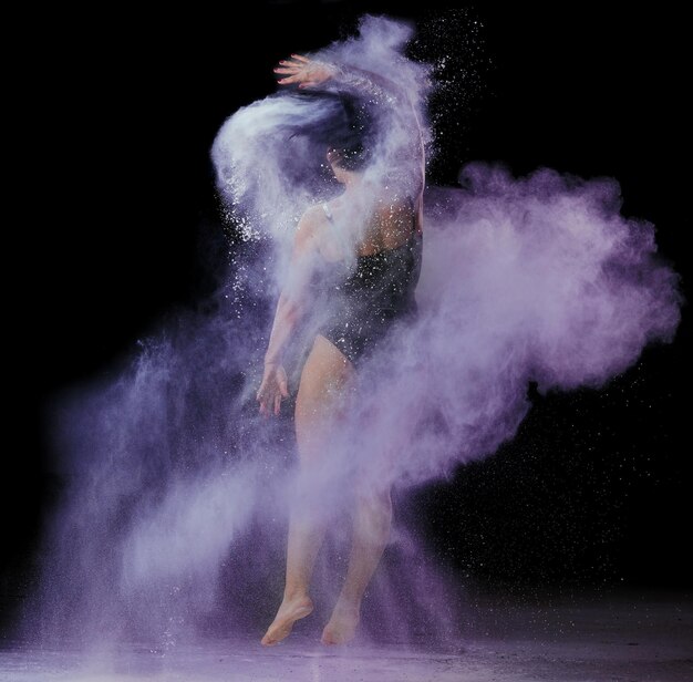 Foto een mooie blanke vrouw in een zwart bodysuit met een sportfiguur danst in een paarse wolk.