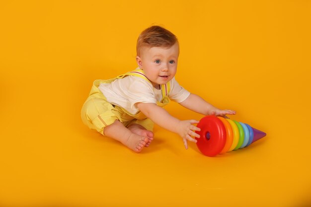 Een mooie, blauwogige kleine jongen in een geel pak speelt een veelkleurige speelgoedpiramide