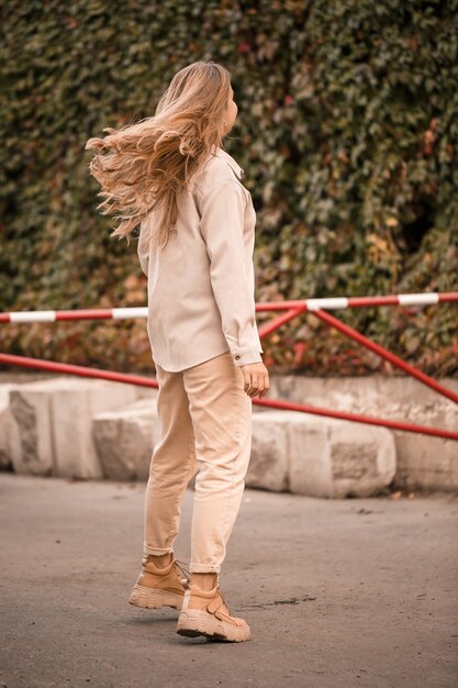 Een mooie blonde jonge vrouw loopt door de straat, ze draagt een spijkerbroek en een beige shirt. Mooi meisje gekleed in casual stijl met een glimlach op haar gezicht voor een wandeling