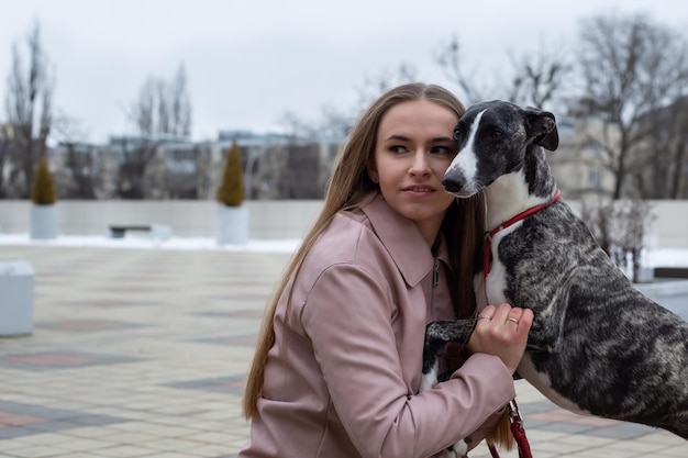 een mooie blonde meid zit bezig met het trainen van een whippet-hond op straat in de stad