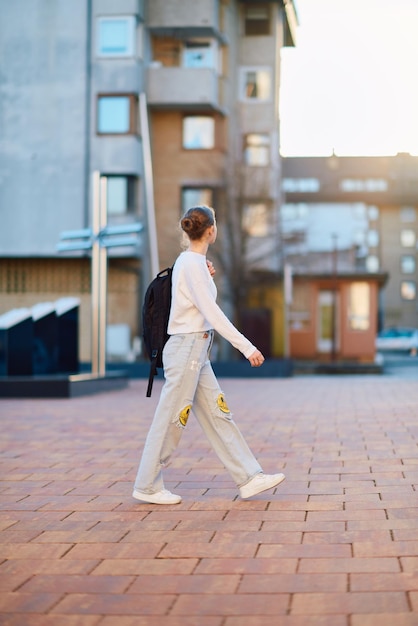 Een mooie blonde tiener keert thuis van school tijdens de zonsondergang met haar school rugzak