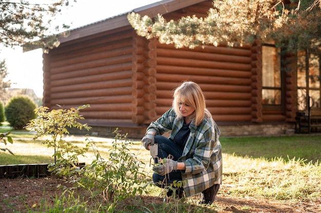 Foto een mooie blonde vrouw in een geruit hemd tuinen in de zonsondergang een vrouw in handschoenen zorgt voor bush...