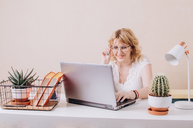 Een mooie blonde vrouw met een bril zit achter een laptop en werkt