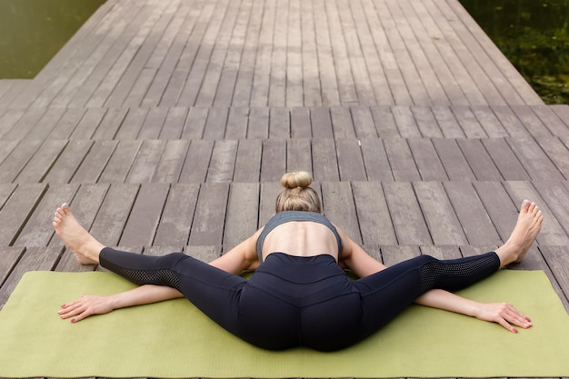 Een mooie blonde vrouw op een houten platform op mat doet yoga en stretching