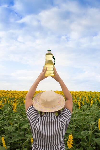 Een mooie boerenvrouw van middelbare leeftijd staat met haar rug en houdt op een zonnige dag flessen gouden zonnebloemolie in haar handen in een oogstveld met zonnebloemen