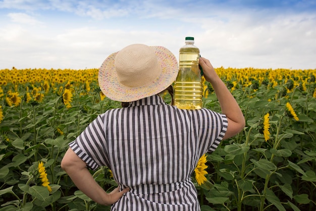 Een mooie boerenvrouw van middelbare leeftijd staat met haar rug en houdt op een zonnige dag flessen gouden zonnebloemolie in haar handen in een oogstveld met zonnebloemen