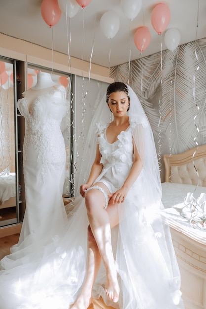Foto een mooie bruid met een lange sluier in haar kamer die een badjas draagt trouwjurk op een mannequin de bruid in de ochtend voor de bruiloftsceremonie