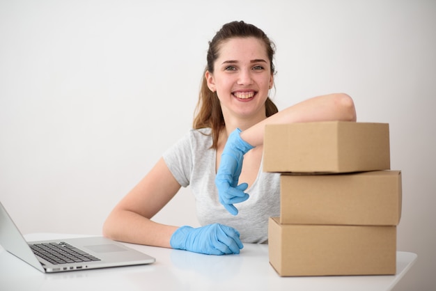 Een mooie brunette met een glimlach, leunend op drie kartonnen dozen, zit in siliconen handschoenen voor een laptop.