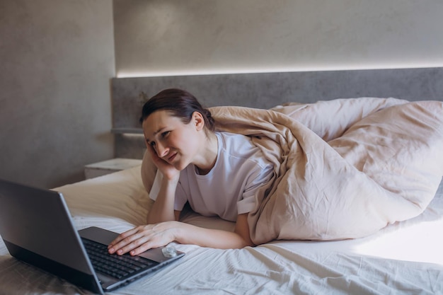 Een mooie brunette vrouw in de slaapkamer op het bed werkt met een laptop
