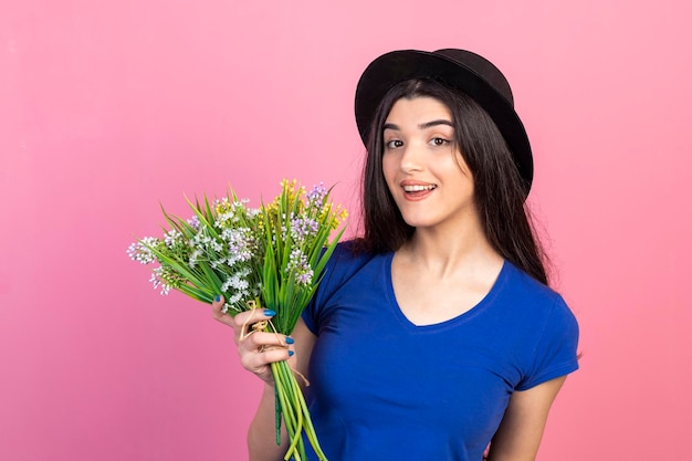 Een mooie dame die een bos bloemen vasthoudt en een hoed draagt met een blauw t-shirt Foto van hoge kwaliteit