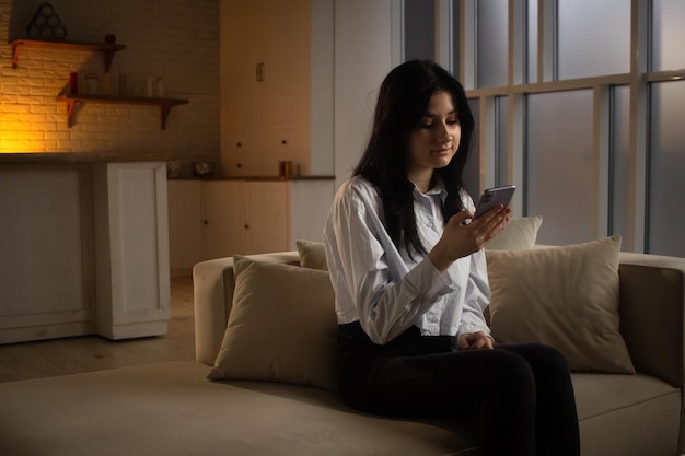 Een mooie donkerharige vrouw zit op een bank en kijkt naar het scherm van haar smartphone waar een jonge vrouw zit