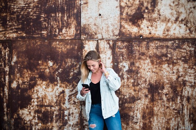 Een mooie en blonde vrouw alleen in de stad die haar telefoon gebruikt en glimlacht - tiener online in sociaal netwerk of sociale media