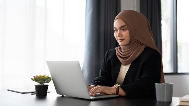 Een mooie en gefocuste duizendjarige Aziatische moslimzakenvrouw werkt op haar laptop aan haar bureau