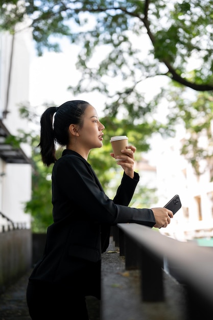 Een mooie en ontspannen duizendjarige Aziatische zakenvrouw drinkt haar middagkoffie buiten