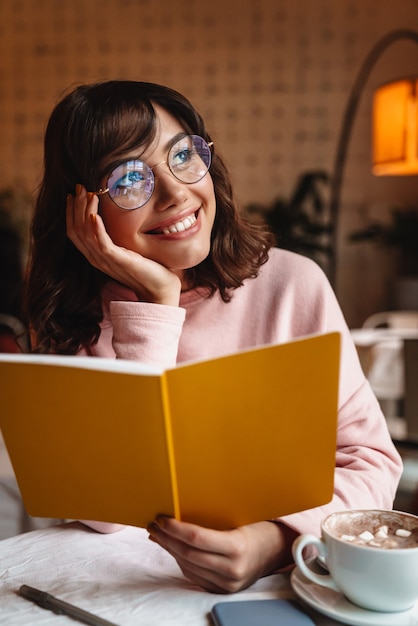 een mooie gelukkig lachende brunette jonge vrouw binnenshuis in café leesboek.